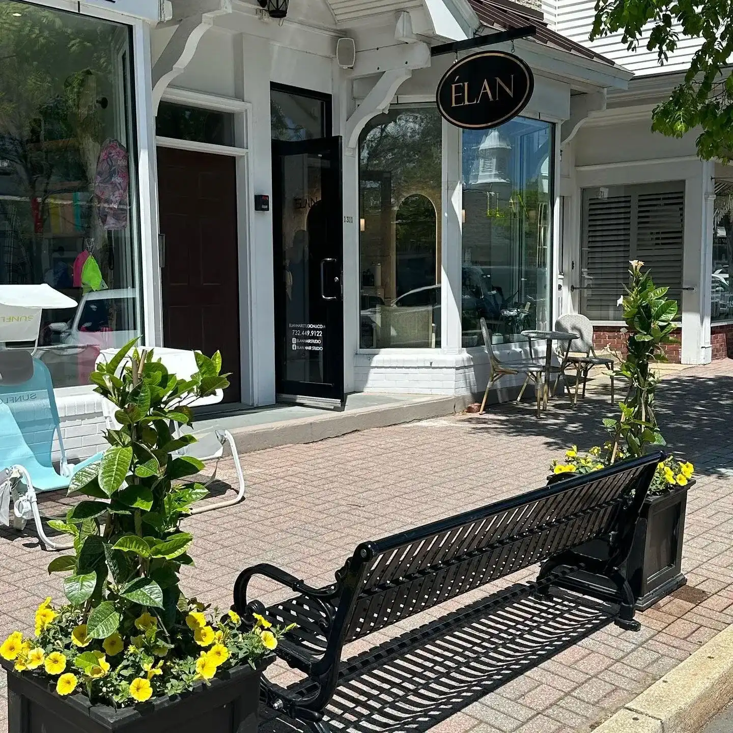 Boutique storefront with a black bench and yellow flowers outside.
