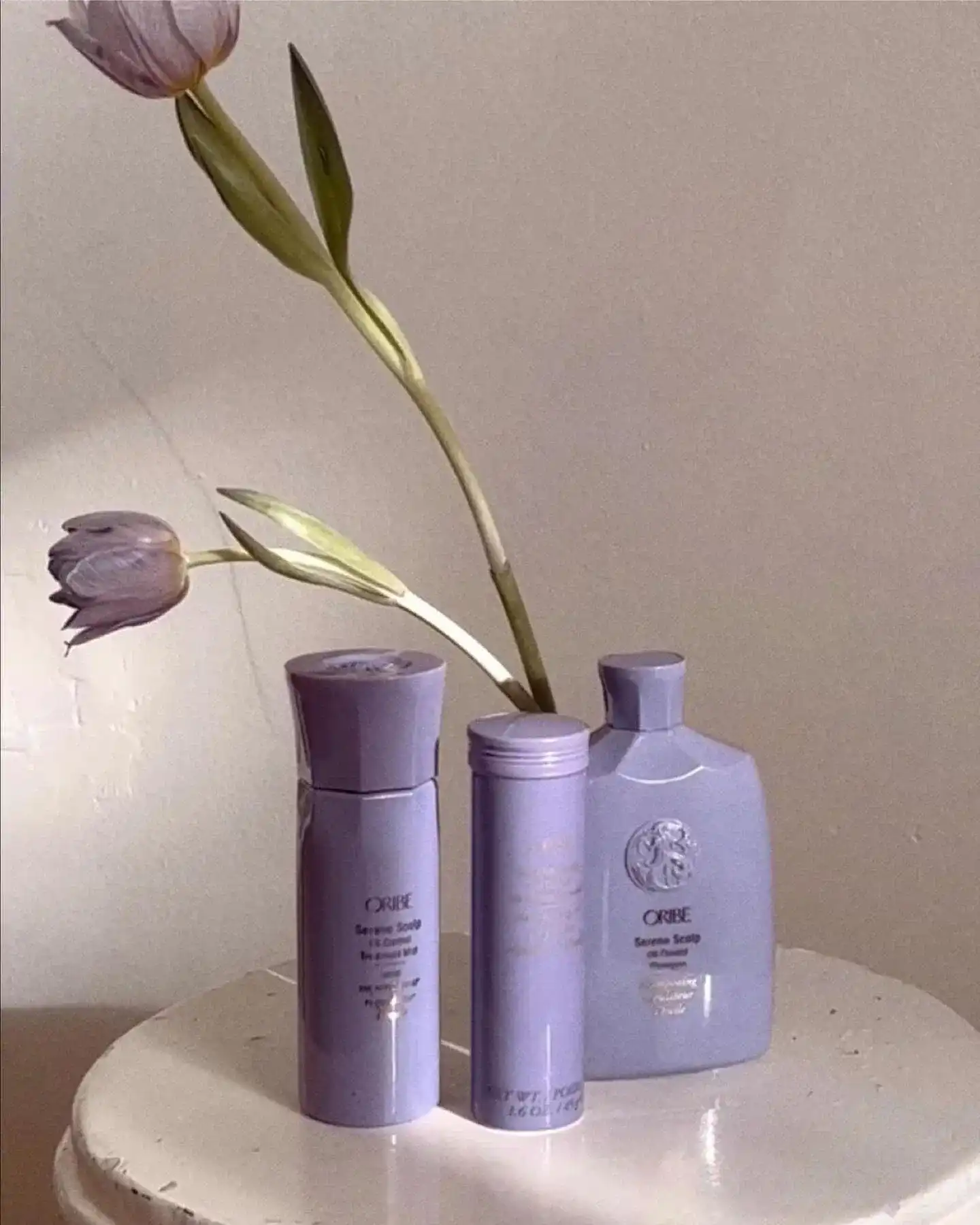 Purple haircare bottles and tulips on a round white table.
