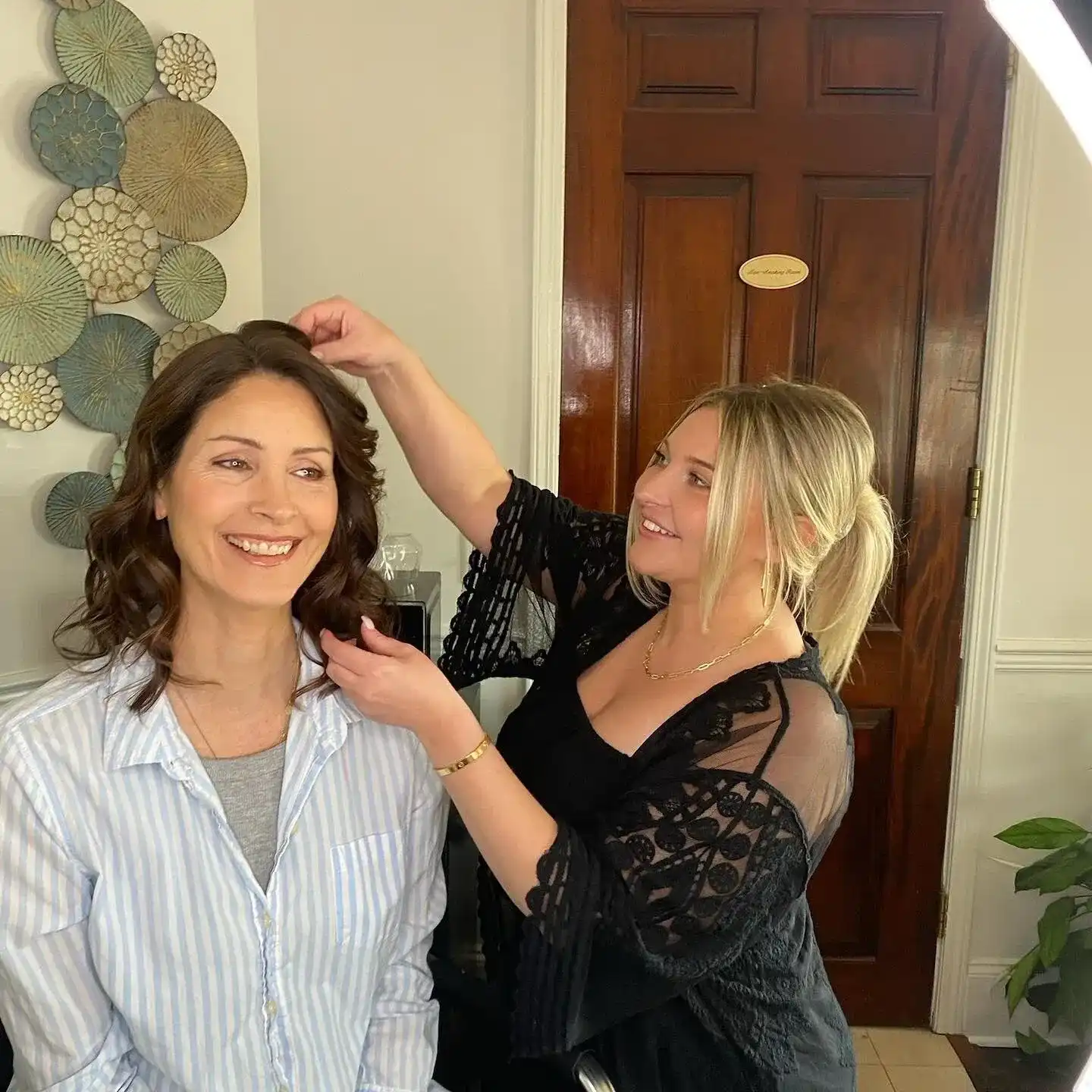 A stylist arranges a woman's hair in a cozy salon setting.